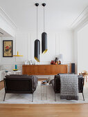 Two black couches, pendant lamps and sideboard in white living room