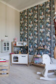 Play kitchen, shelves and rocking horse in child's bedroom with colourful wallpaper