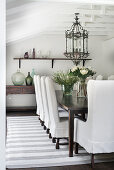 Loose-covered chairs, vintage lantern light fitting above dining table and antique console table in dining room
