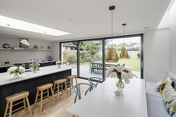 White dining table, fitted bench and open-plan kitchen with island counter and terrace doors