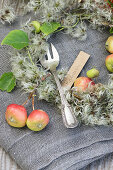 Kuchengabel mit Namensschild zwischen kleinen Äpfeln und Clematis