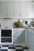 Helle Einbauküche mit weißen Wandfliesen und schwarz-weiß kariertem Linoleumboden
