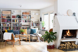 Regalwand, Plastik-Couch mit bunten Kissen, Couchtisch und Sessel im Wohnzimmer, im Vordergrund Kamin