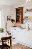 Old glass-fronted cabinet in white kitchen with white-tiled walls
