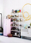 Open shelf with crockery next to pink fridge, yellow hose as wall decoration