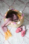 Knitted scarf in basket with pompoms next to ladies' shoes