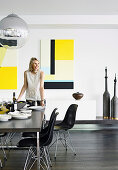 Woman sets the table in the modern dining room with yellow pictures