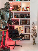 Suit of armour and leather chair in front of shelves holding eclectic collection of items