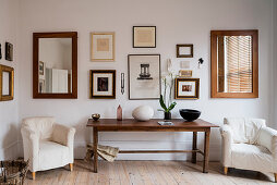 Orchidee and wooden bowl on farmhouse table flanked by pair of armchairs, assorted artwork and mirrors hang on the wall