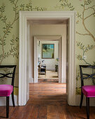 Wall paper around doorway flanked by pair of dining chairs upholstered in velvet