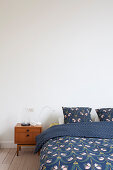 Bed with blue bed linen and bedside cabinet in mid-century modern style