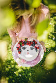 Girl holding white fondant cake decorated with face made from berries and icing