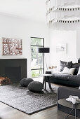 Living room with anthracite-colored furnishings: upholstered sofa, floor lamp by the window, pouf and coffee table in front of the fireplace