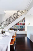 Laid dining table with classic chairs, stairs and bookcase in the background