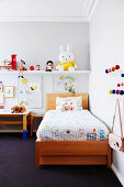 Wooden bed with colorful bedclothes, a shelf with play figures in the children's room