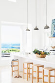 Küchentheke mit Barhopckern aus Holz und Pendelleuchten im Hintergrund Fenster mit Meerblick