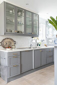 Kitchen counter with pale grey cupbards below wall cabinets with glass doors
