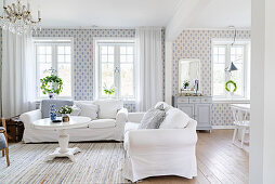Weiße Hussensofas und runder Tisch in offenem Wohnraum mit blau-weißer Tapete
