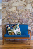 Wooden sofa with blue upholstery and colourful scatter cushion against stone wall