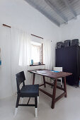 Wooden table and two chairs next to lattice window in front of black fabric wardrobe