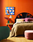 Double bed with headboard and bedside table against orange wall with picture