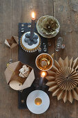 Weihnachtliche Tischdeko mit goldenem Porzellan, Papierblumen, Stern und grauen Kerzen auf Schieferplatte