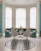 Seating, round table and labyrinth pattern on floor in white and sky-blue interior with bay window