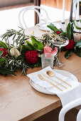 Gesteck mit Protea und Olivenzweigen auf gedecktem Tisch