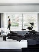 Minimalistischer Schlafraum in Schwarz und Weiß mit Designermöbeln, Person vor Fenster