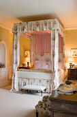 Four-poster bed with chintz curtains in olive-green bedroom in English manor house