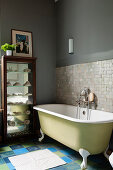 Pale green, free-standing bathtub against mosaic wall tiles in grey bathroom