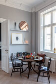 Round dining table with wooden chairs in corner of renovated period apartment