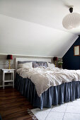 Bett mit blauem Volant unter der Dachschräge im Schlafzimmer