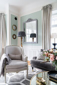 Armchair and sofa in light-flooded living room with pastel-green walls