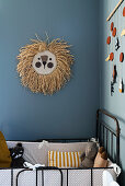 Raffia lion head on blue-grey wall above cot in nursery