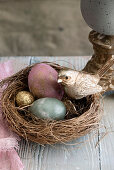 Nest mit bunten Eiern und goldfarbenem Vogel als Osterdekoration