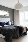 Blanket on double bed with button-tufted headboard against dark grey wall