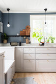 Weiße Küchenzeile mit Marmor-Arbeitsplatte vor Fenster in Küche mit grau-blauer Wand