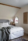 Bed with grey headboard in attic bedroom of renovated Swedish house