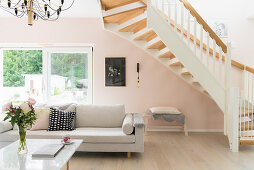 Coffee table and white sofa below staircase in living room with pink wall