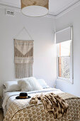 Beigefarbener Ethno-Wandbehang über Bett mit weißem Fellkissen