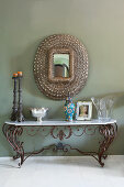 Antique, wrought-iron console table with marble top below mirror on wall