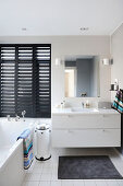Elegantes Badezimmer mit Waschbeckenunterschrank, schwarze Jalousie und Badewanne