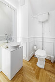 Washstand and toilet in white bathroom with parquet flooring