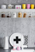 Storage jars and crockery on metal shelves on grey concrete kitchen wall