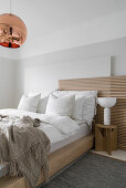 Double bed with slatted wooden headboard in bedroom with copper-coloured spherical lamp