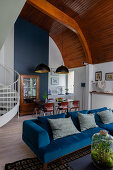 Blue velvet sofa, table in dining area and antique dresser below arched wooden ceiling
