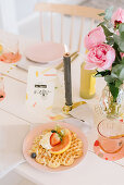 Waffles and fruit on table festively set with candle and vase of peonies