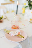 Table festively set with place cards and gold cutlery on pale pink plate