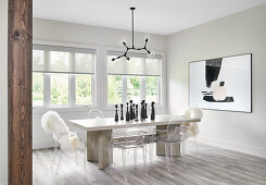 White dining room with wooden table, Ghost chairs, black pendant and modern art on wall